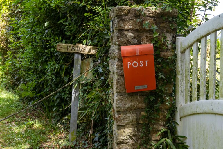 Briefkasten am Haus oder Grundstücksgrenze – roter Briefkasten an einer Steinmauer mit Gartentor