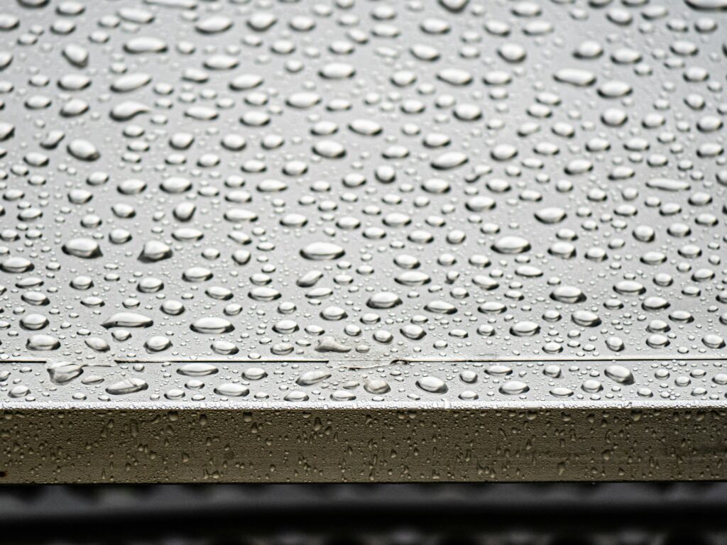 Schwitzwasser am Dach – Kondenswassertropfen auf einer kalten metallischen Oberfläche als Sinnbild für Kondensation an Bauteilen