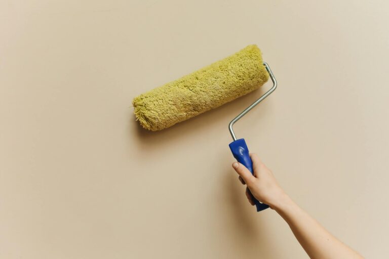 Buntsteinputz streichen – gelber Lackroller streicht beigefarbene Wand