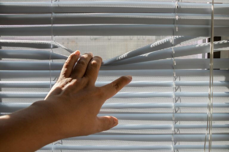 Plissee reparieren – Hand öffnet ein weißes Fensterplissee