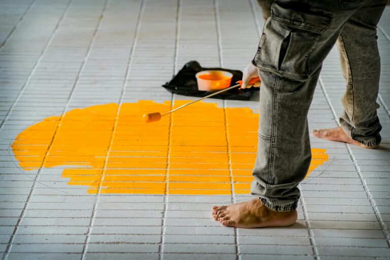 PVC-Boden streichen – Person streicht hellen Bodenbelag mit Roller