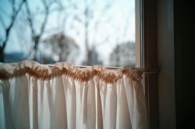 Rollo an Gardinenschiene befestigen – weißer Vorhang am Fenster mit Sonnenlicht