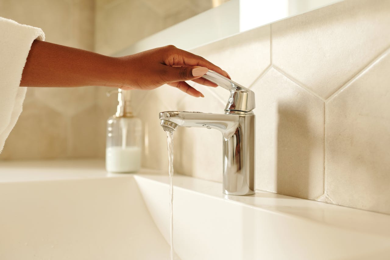 Wasserhahn aufdrehen Richtung – Hand bedient einen Chrom-Hahn im Badezimmer