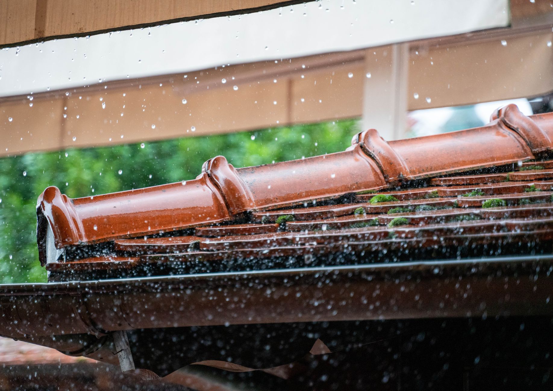 Dachrinne reinigen – Regen an einer Terracotta-Dachkante mit Rinne und Moos