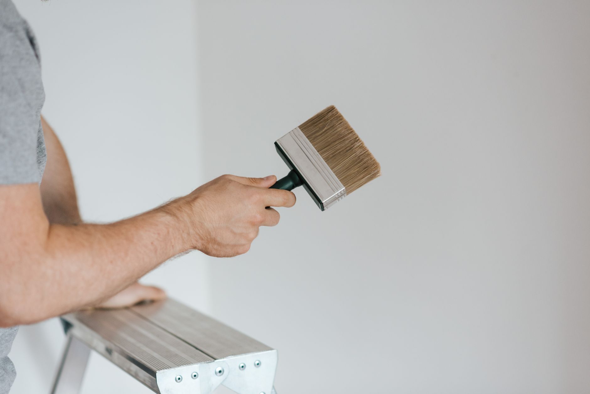 Wände streichen ohne Streifen – Heimwerker mit Flächenpinsel an einer weißen Wand