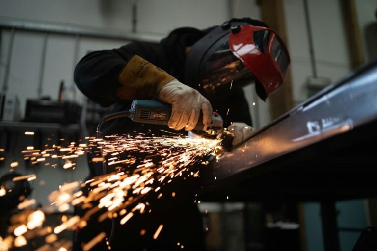 Metalloberflächen professionell behandeln und optimieren: Verfahren & Tipps für Bauprofis A person wearing a welding helmet grinding a metal beam with sparks flying